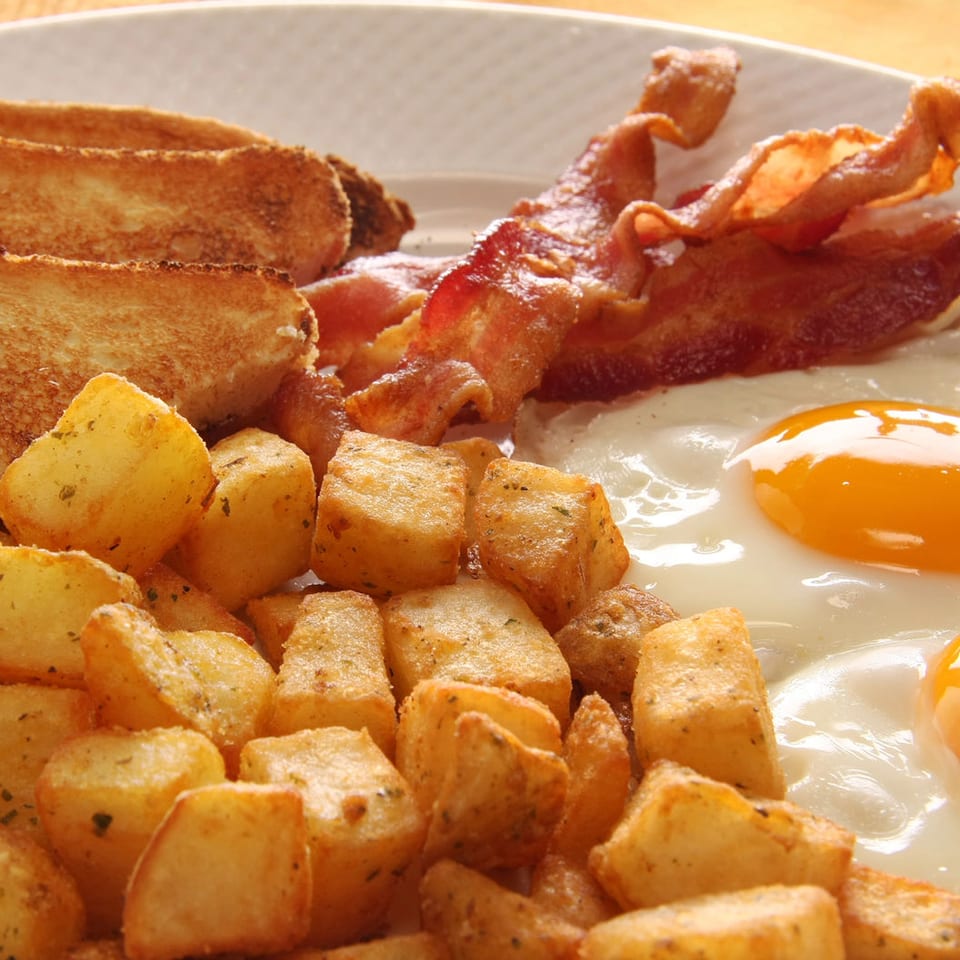 Breakfast plate with toast, crispy bacon, golden home fries, and two sunny-side-up eggs.