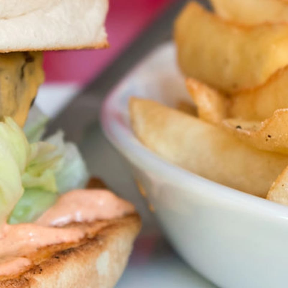 Cheeseburger with lettuce, tomato, and sauce beside a bowl of golden fries.