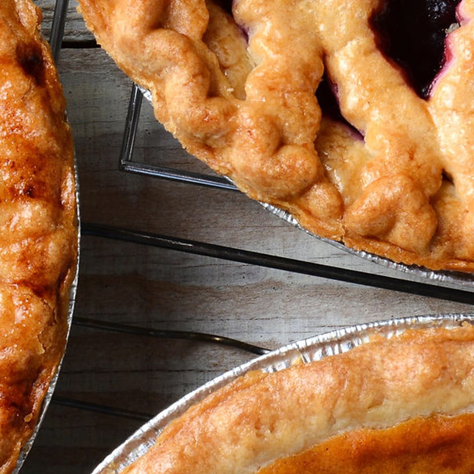 Close-up of three golden lattice-crust pies cooling on wire racks, including fruit-filled and custard pies.